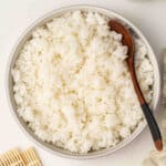 Bowl filled with fluffy sushi rice and a wooden spoon, ready to use for rolls or bowls.