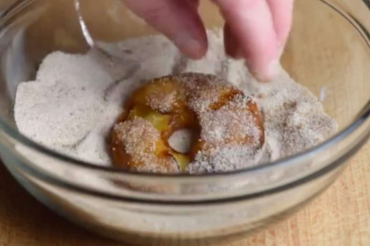 fried apple ring being coated in cinnamon-sugar