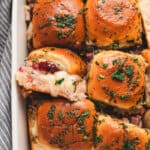 Golden baked cranberry turkey sliders topped with parsley butter glaze in a white baking dish.