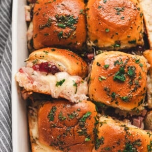 Golden baked cranberry turkey sliders topped with parsley butter glaze in a white baking dish.