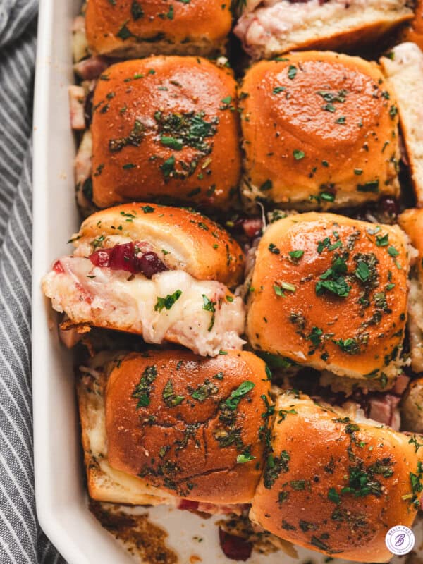 Golden baked cranberry turkey sliders topped with parsley butter glaze in a white baking dish.