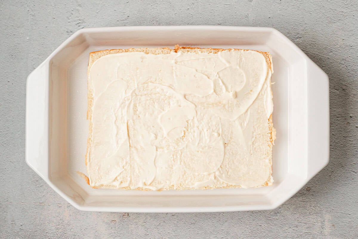 Bottom halves of slider rolls spread with mayonnaise in a white baking dish.