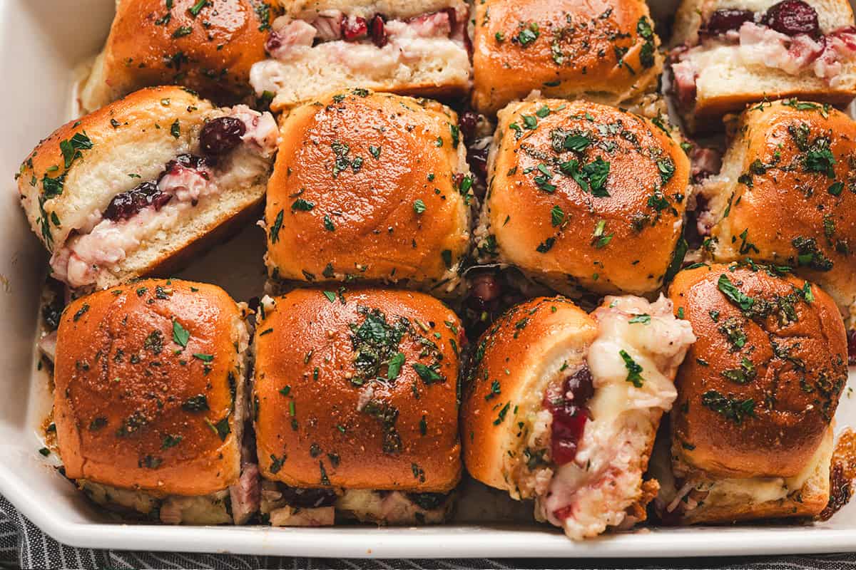 Baked cranberry turkey sliders cut apart in the baking dish, showing melted cheese and cranberry filling.