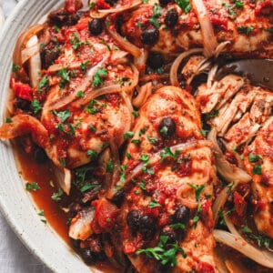 Close-up of slow cooker tomato balsamic chicken served on a platter with onions, black beans, and fresh parsley.