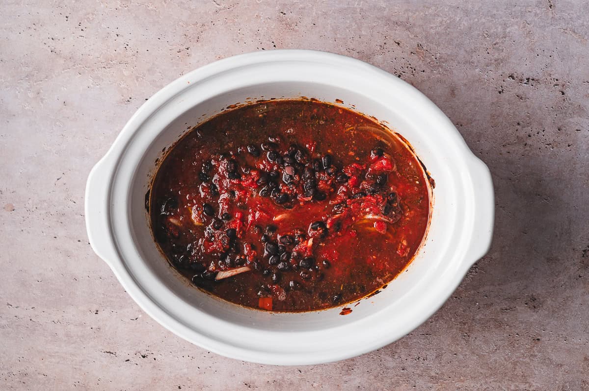 Overhead view of tomato balsamic chicken cooking in a slow cooker with black beans, onions, and tomato sauce.