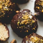 Close-up of Dubai chocolate truffles coated in dark chocolate and topped with crushed pistachios and flaky sea salt, one truffle cut open to show the creamy pistachio kataifi filling.