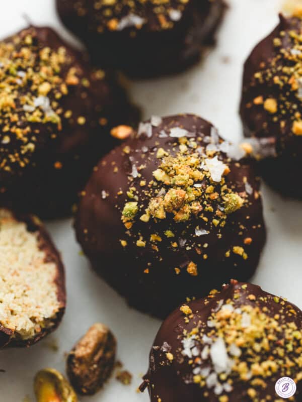Close-up of Dubai chocolate truffles coated in dark chocolate and topped with crushed pistachios and flaky sea salt, one truffle cut open to show the creamy pistachio kataifi filling.