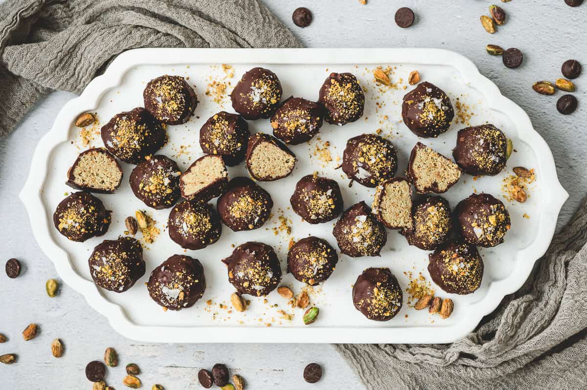 Dubai chocolate truffles arranged on a white serving platter, some cut in half to show pistachio filling, surrounded by pistachios and chocolate chips.