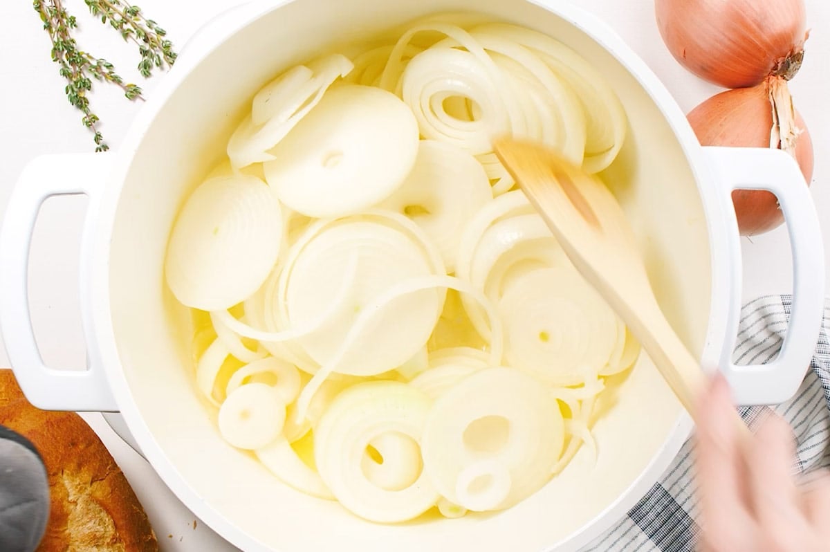 sliced onions being stirred in pot with butter