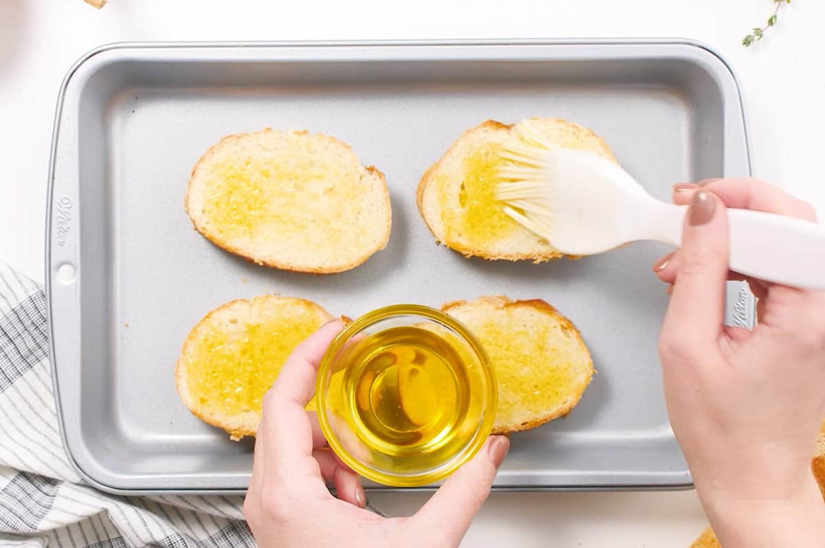 olive oil being brushed on french bread slices