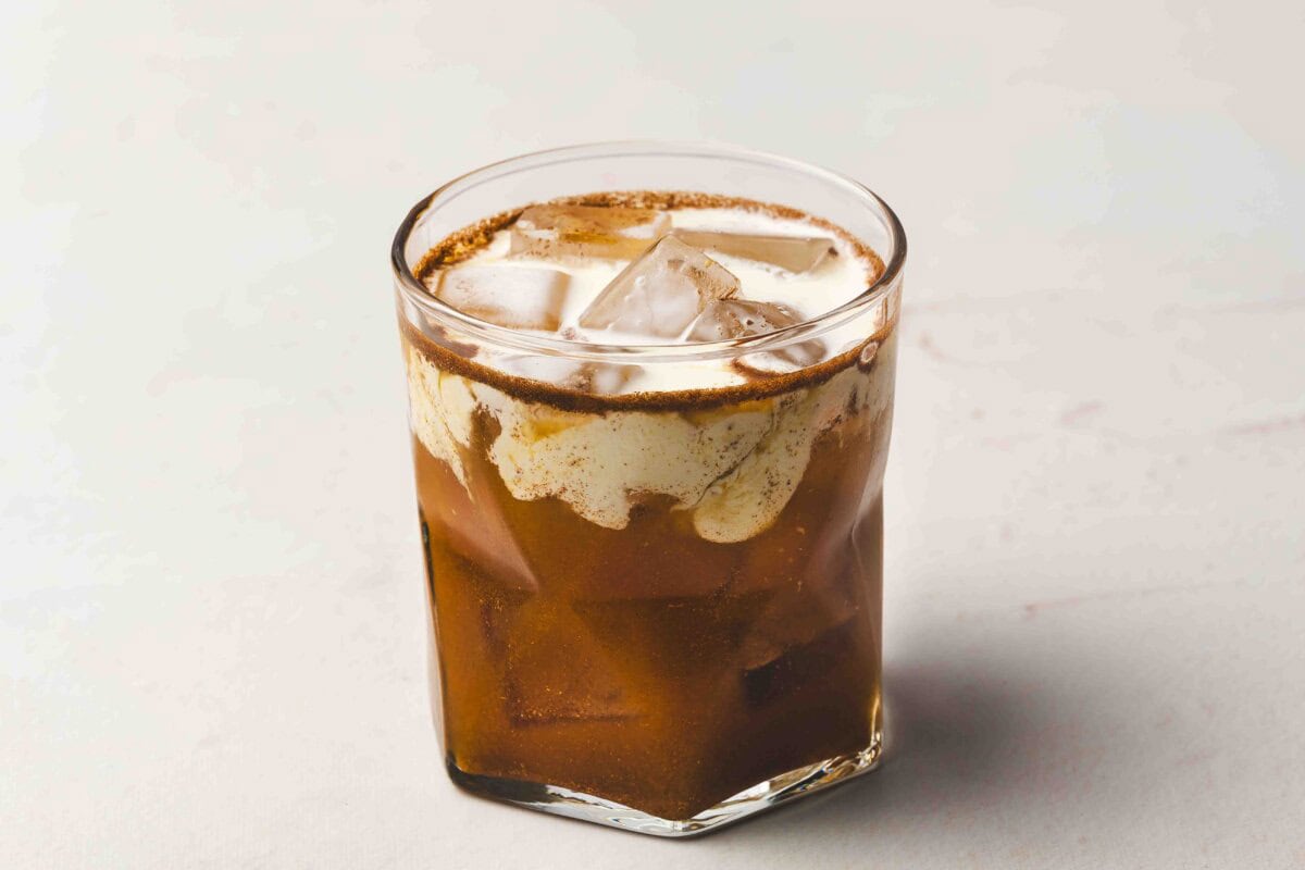 Close-up of a freshly mixed pumpkin pie White Russian in a glass with ice, showing swirls of cream blending into the spiced pumpkin coffee mixture for a rich, marbled look.