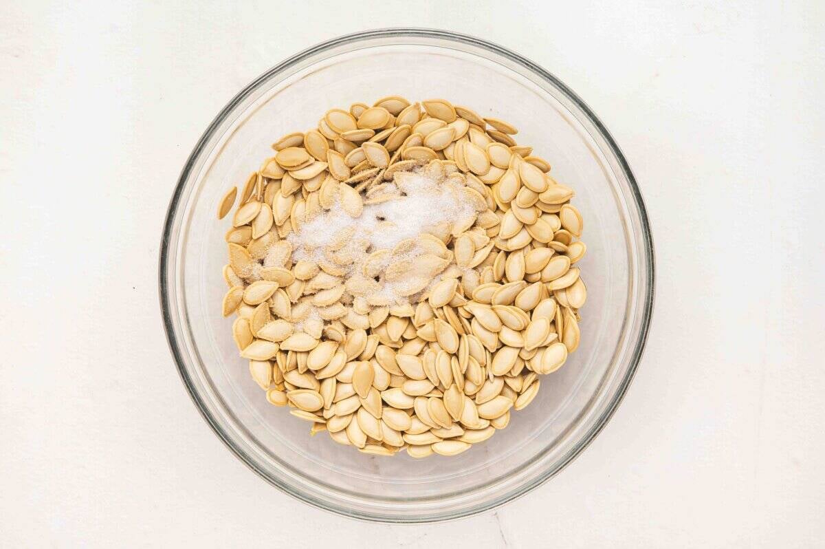 Raw pumpkin seeds in a glass bowl topped with coarse kosher salt before tossing