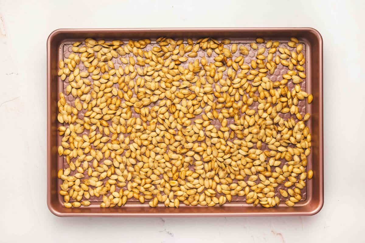 Pumpkin seeds roasting on a baking sheet, turning golden brown as they toast in the oven.