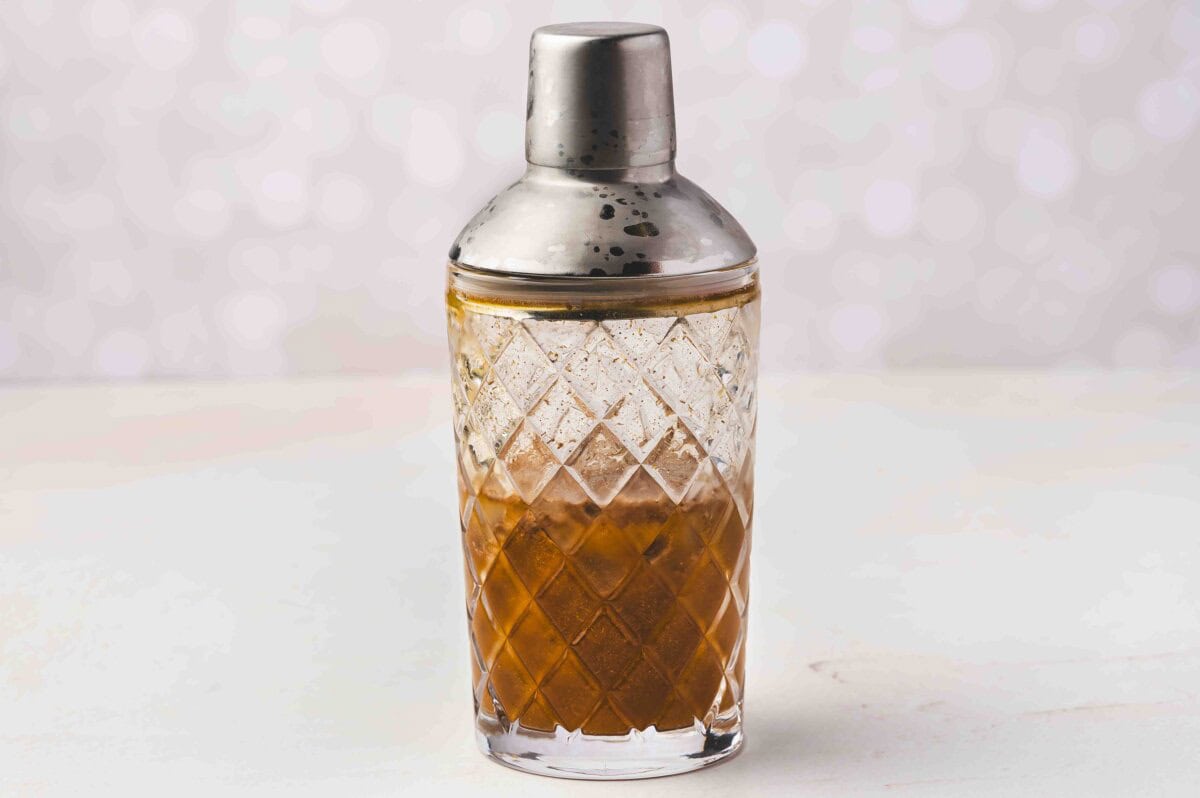 A cocktail shaker filled with the pumpkin, coffee liqueur, and vodka mixture ready to be shaken for a pumpkin pie White Russian.