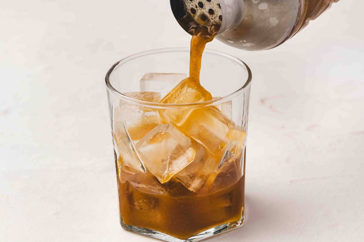 Pouring the spiced pumpkin and coffee liqueur mixture from the shaker over ice in a glass to start layering the pumpkin pie White Russian.