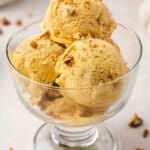 Three scoops of no-churn pumpkin pie ice cream in a glass dessert bowl topped with chopped candied pecans.