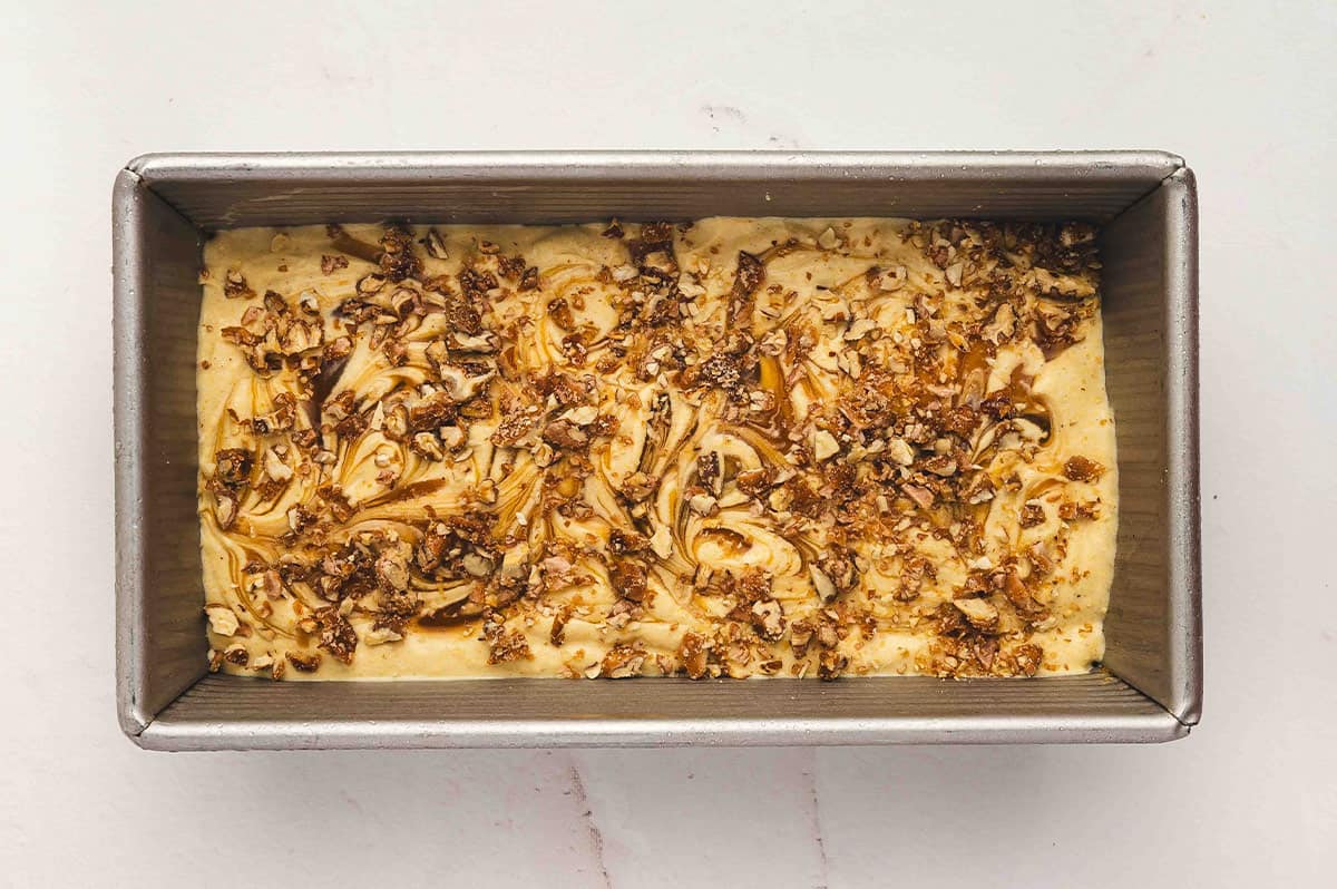 Loaf pan filled with pumpkin ice cream mixture topped with caramel swirls and chopped candied pecans before freezing.