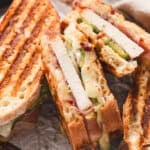 Close-up of sliced prosciutto-wrapped turkey panini showing melted Swiss cheese, avocado, and grill marks on toasted bread.