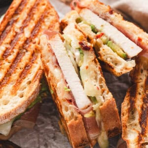 Close-up of sliced prosciutto-wrapped turkey panini showing melted Swiss cheese, avocado, and grill marks on toasted bread.