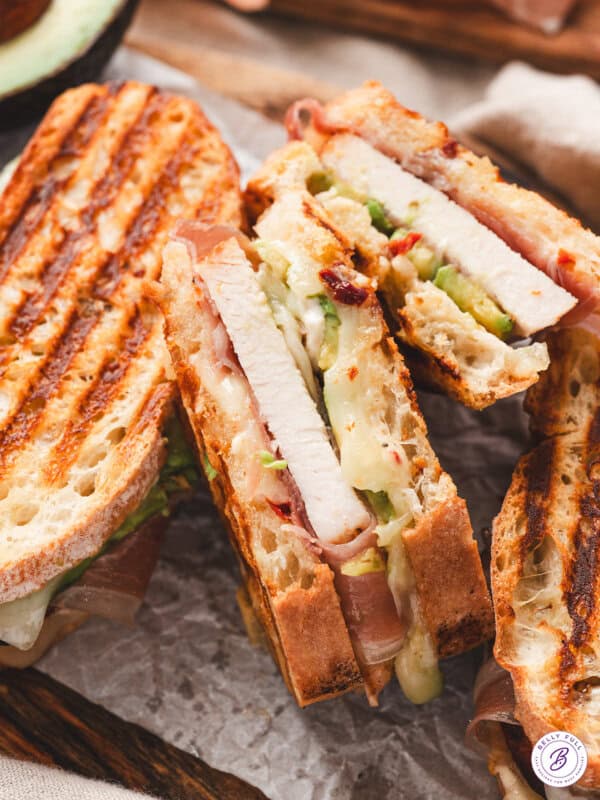 Close-up of sliced prosciutto-wrapped turkey panini showing melted Swiss cheese, avocado, and grill marks on toasted bread.