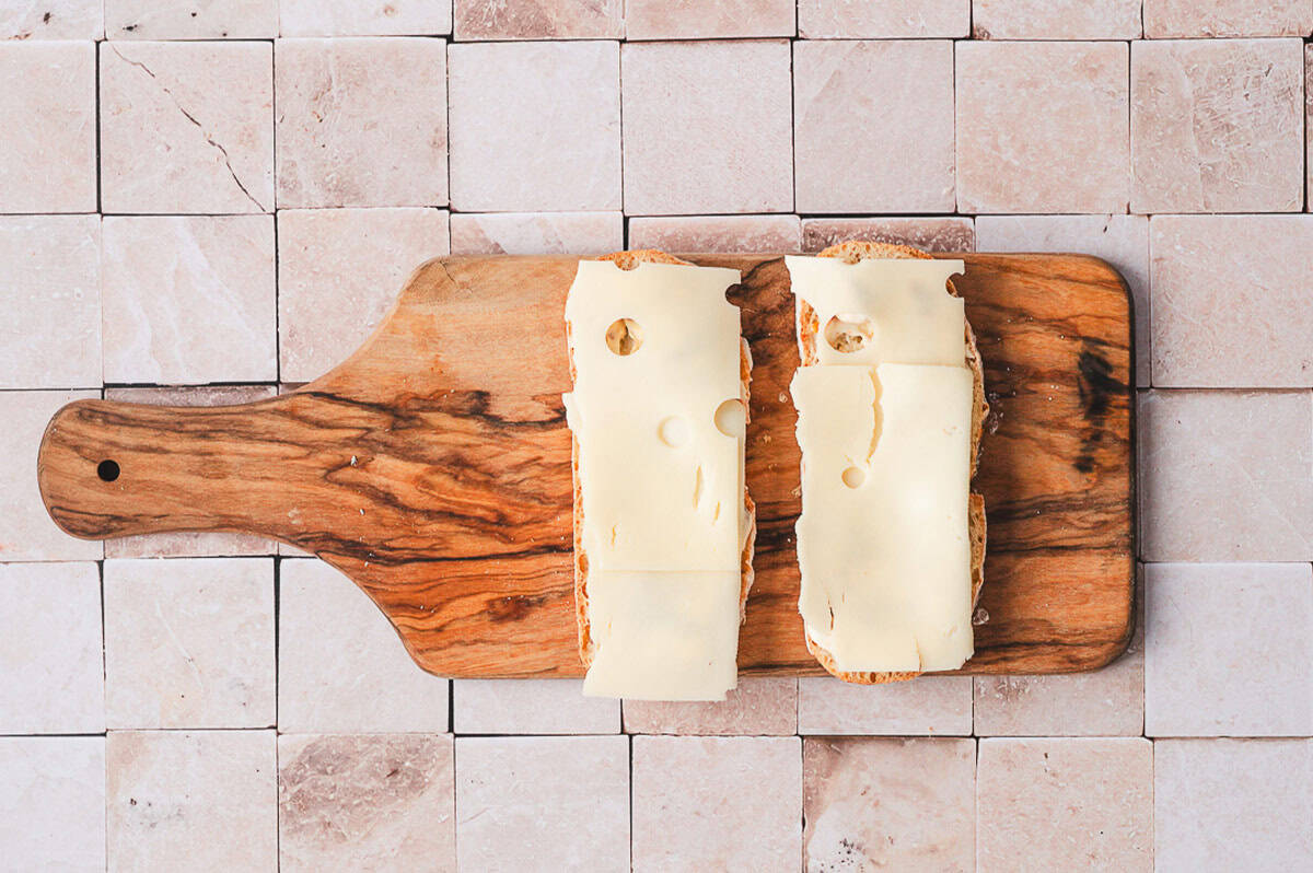 Two slices of Italian bread topped with slices of Swiss cheese on a wooden cutting board.