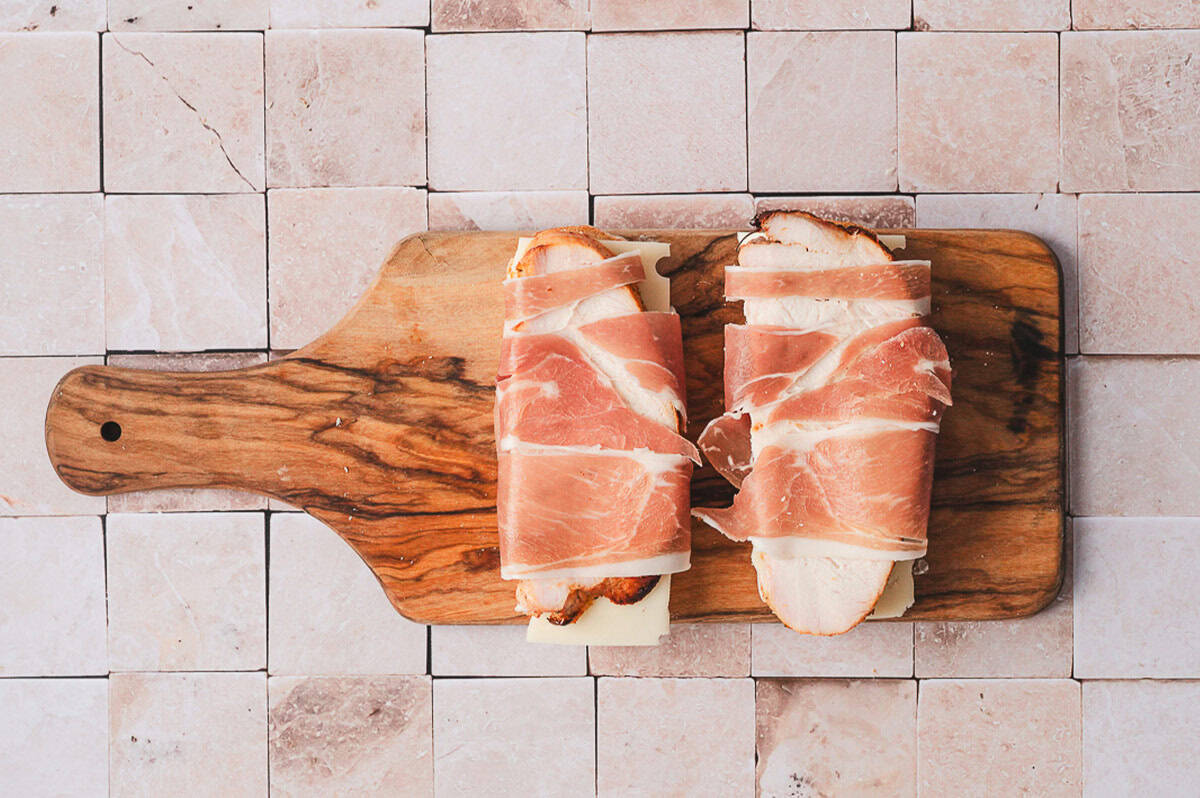 Two stacks of prosciutto-wrapped turkey breast placed on top of the first cheese layer on bread.