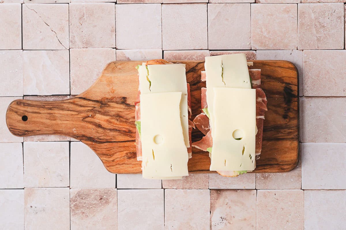 Two open-faced sandwiches layered with prosciutto-wrapped turkey, avocado, and a second slice of Swiss cheese.