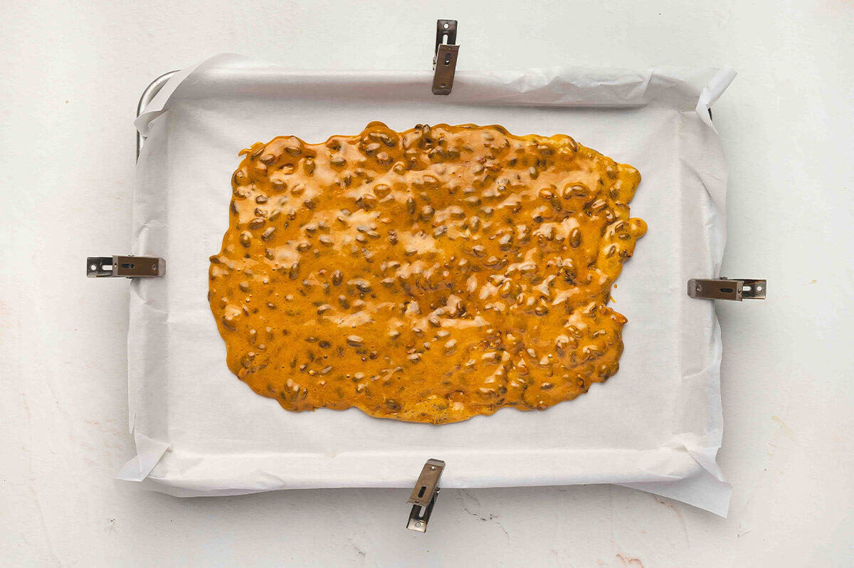 Hot pumpkin seed brittle mixture spread out evenly on a parchment-lined baking sheet to cool.