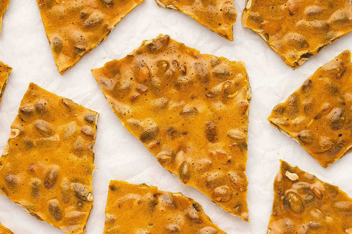 Cooled and hardened pumpkin seed toffee brittle broken into large golden shards on parchment paper.