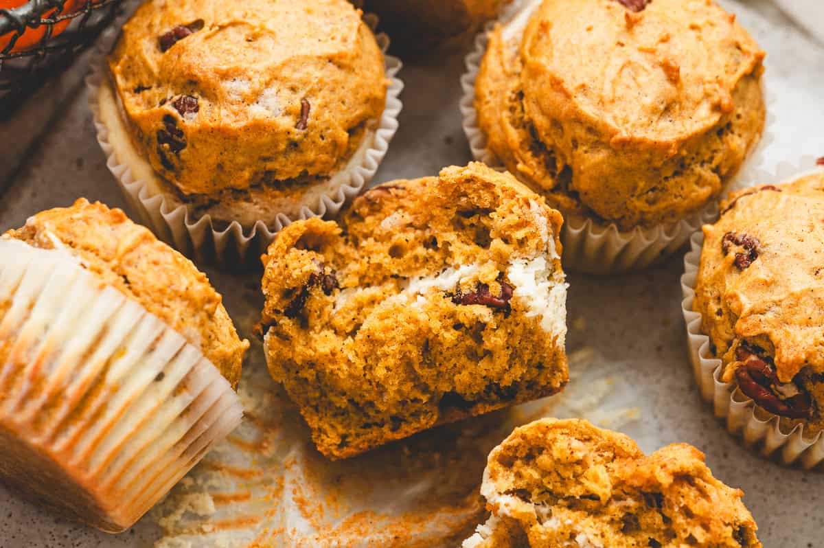 Pumpkin cream cheese muffins with one sliced open to reveal the creamy cheesecake center.