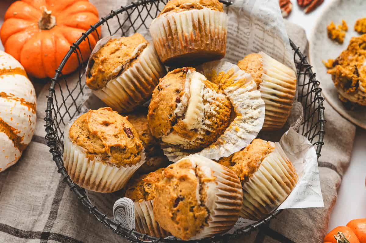 A basket filled with pumpkin cream cheese muffins surrounded by small pumpkins for a fall themed display.
