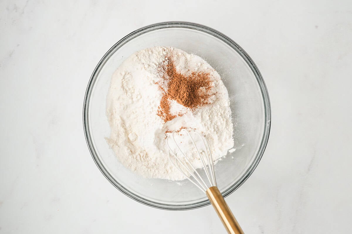 A glass bowl with flour and pumpkin pie spice being whisked together for the muffin batter.