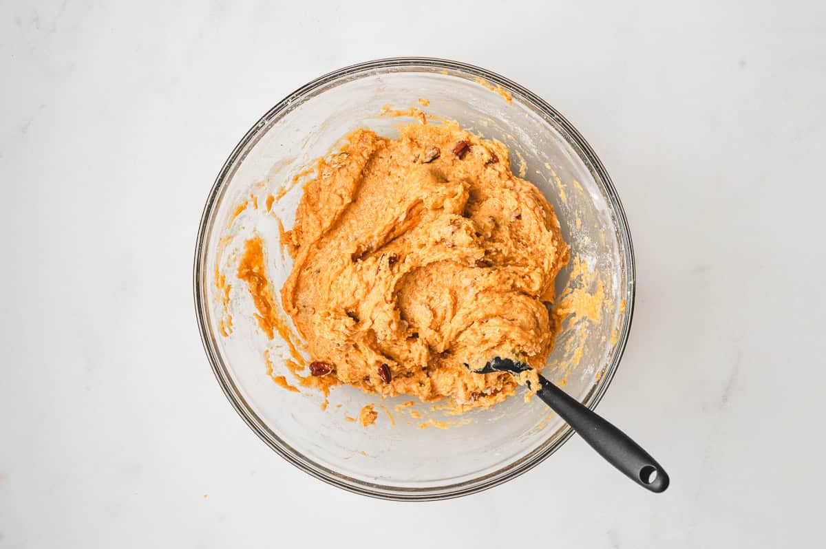 Pumpkin muffin batter with chopped pecans folded in inside a glass mixing bowl.