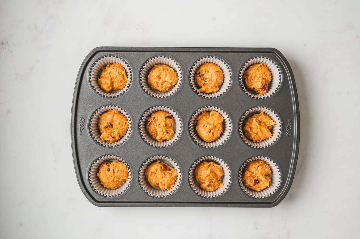 Paper liners in a muffin pan filled halfway with pumpkin muffin batter.