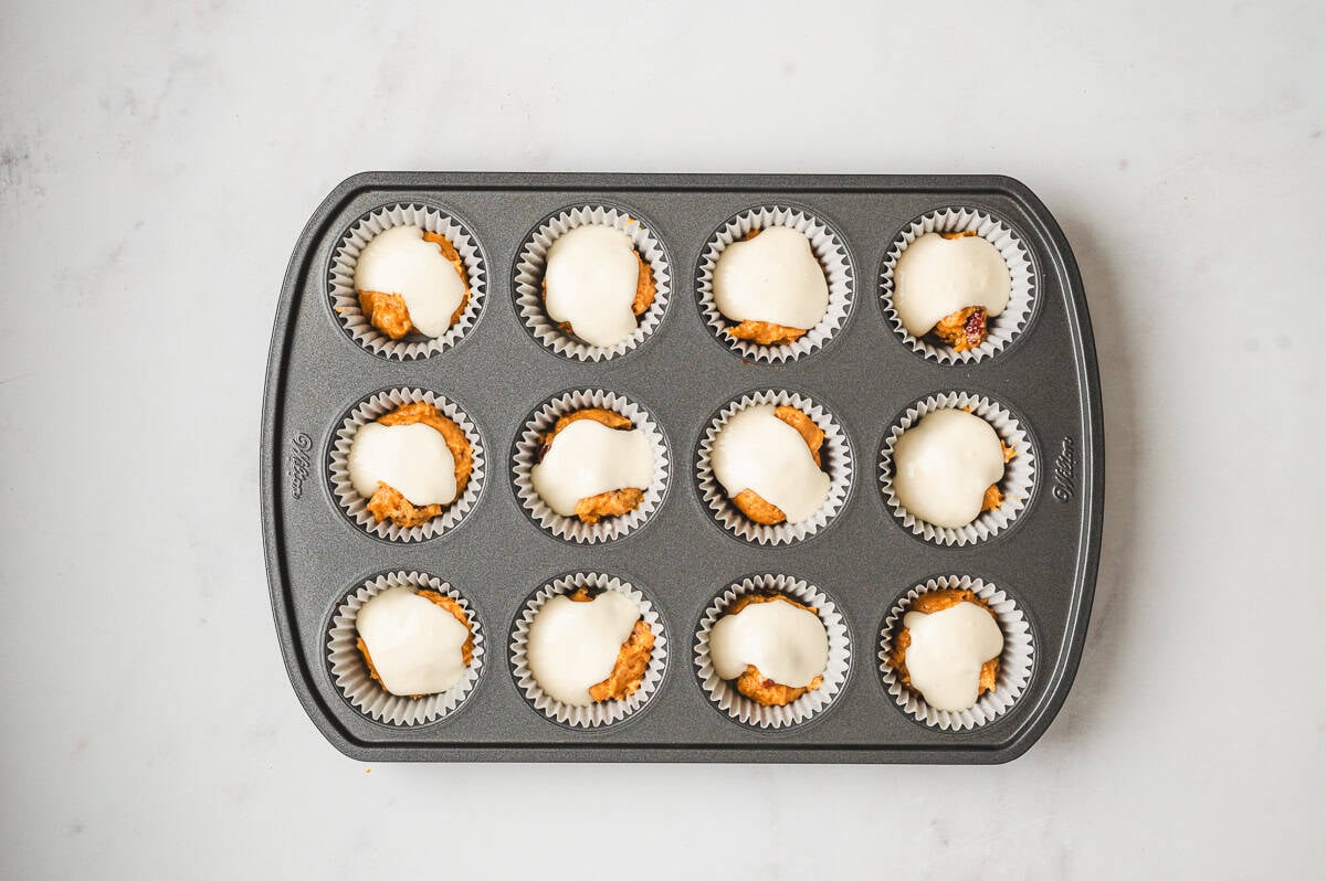 Muffin pan with dollops of cream cheese filling placed on top of the first layer of pumpkin batter.