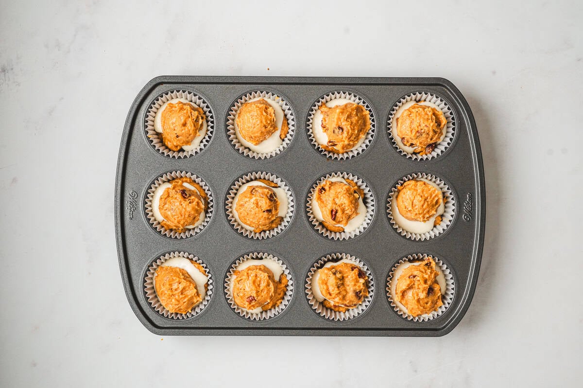 Muffin tin showing the cream cheese filling covered with the final layer of pumpkin muffin batter.