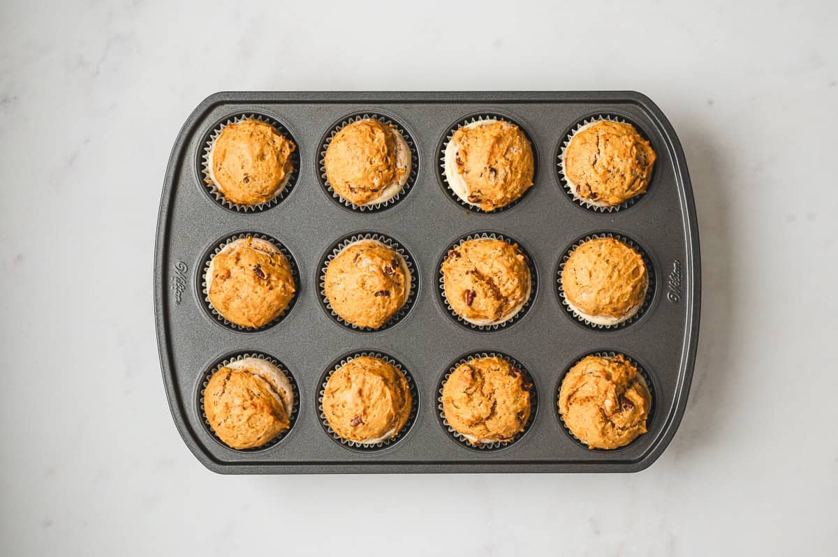 Freshly baked pumpkin cream cheese muffins cooling in a muffin tin.