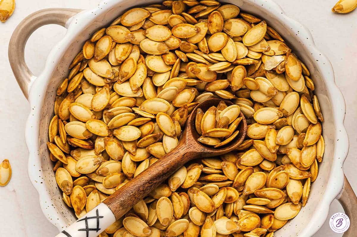 Toasted roasted pumpkin seeds in a white bowl with a wooden spoon, ready to eat