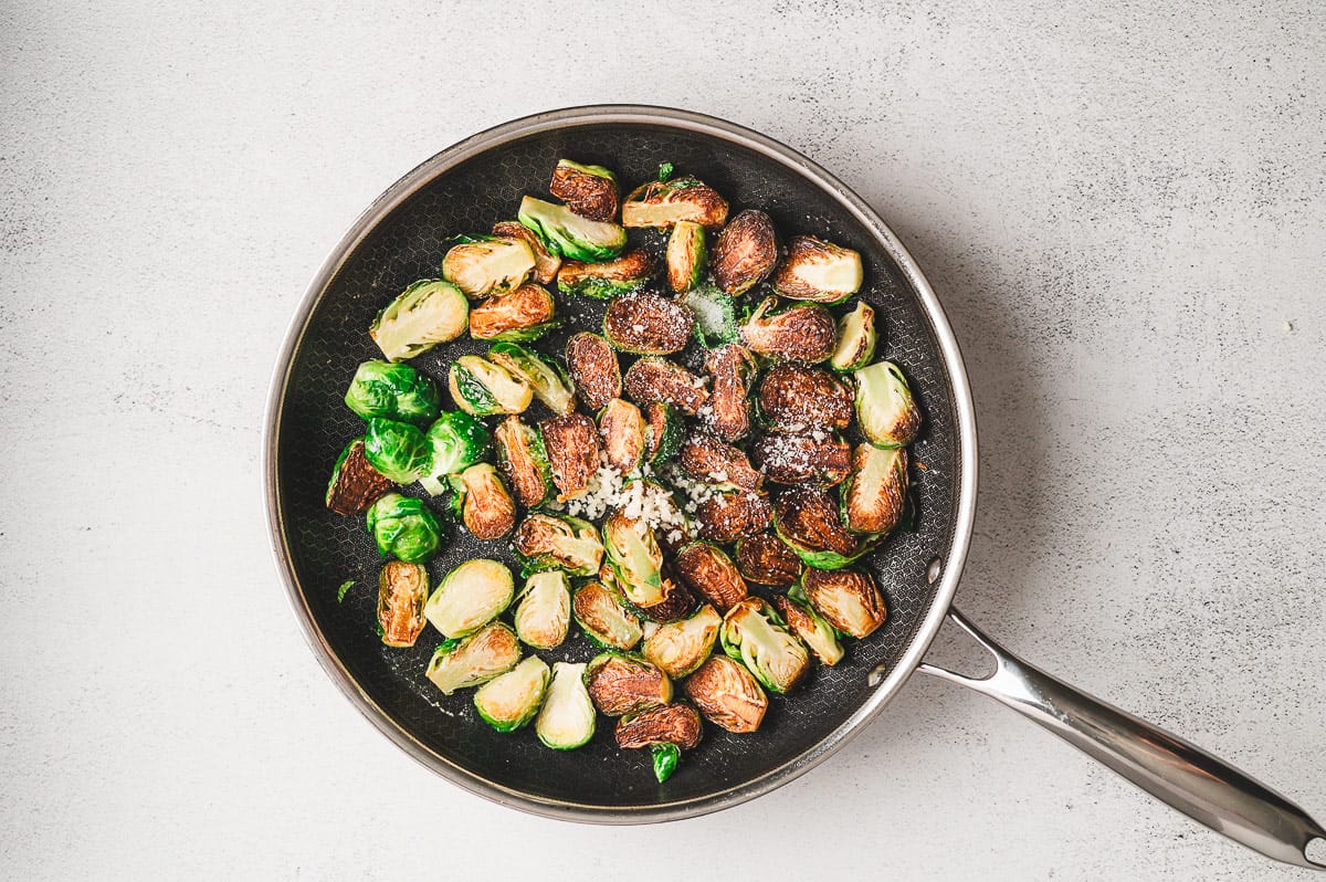 Brussels sprouts seared until browned on one side in a skillet, sprinkled with minced garlic and coarse salt.