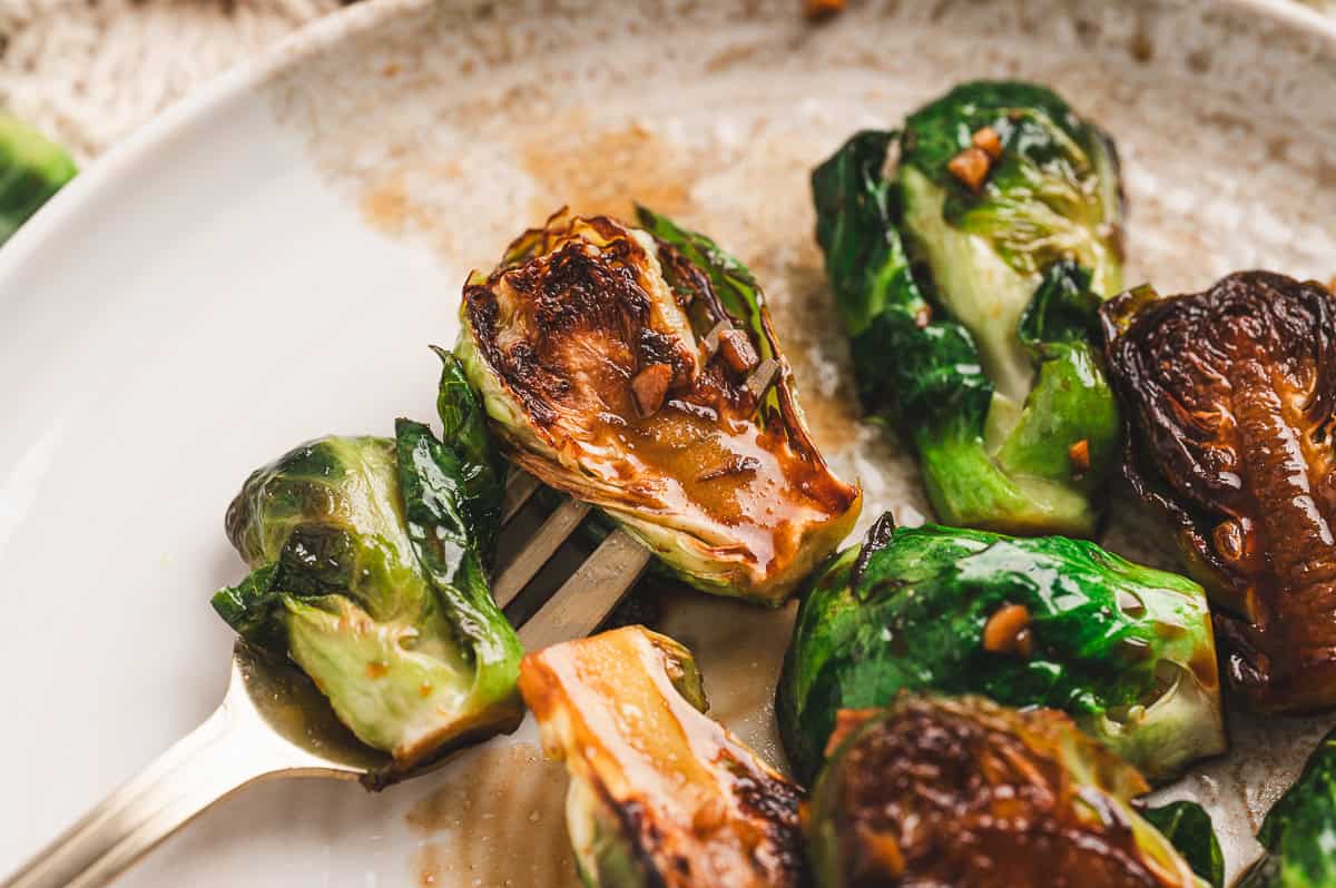 Fork holding a halved Brussels sprout with caramelized edges and glossy molasses glaze on a white plate.