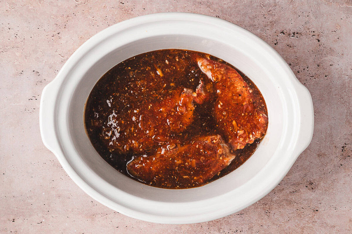 Browned pork ribs coated with orange marmalade hoisin sauce inside a slow cooker before cooking