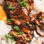 Close-up of slow cooker orange marmalade pork served over white rice, garnished with scallions and orange slices.