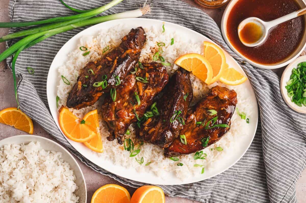 Platter of slow cooker orange marmalade pork with white rice, orange slices, scallions, and extra sauce on the side.