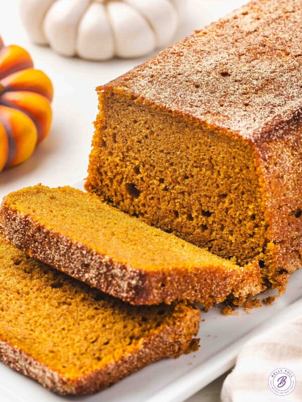 Sliced snickerdoodle pumpkin bread on a white platter, showing its soft texture and cinnamon sugar crust.