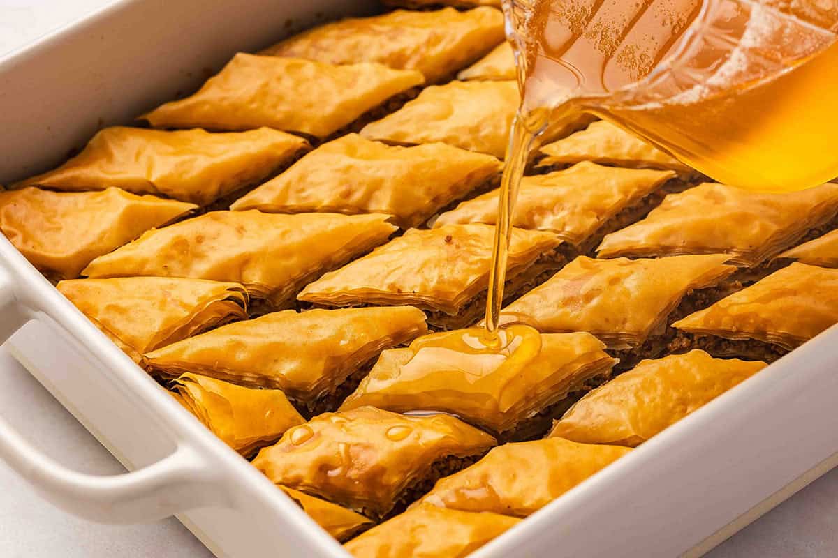 syrup being poured over baklava in pan