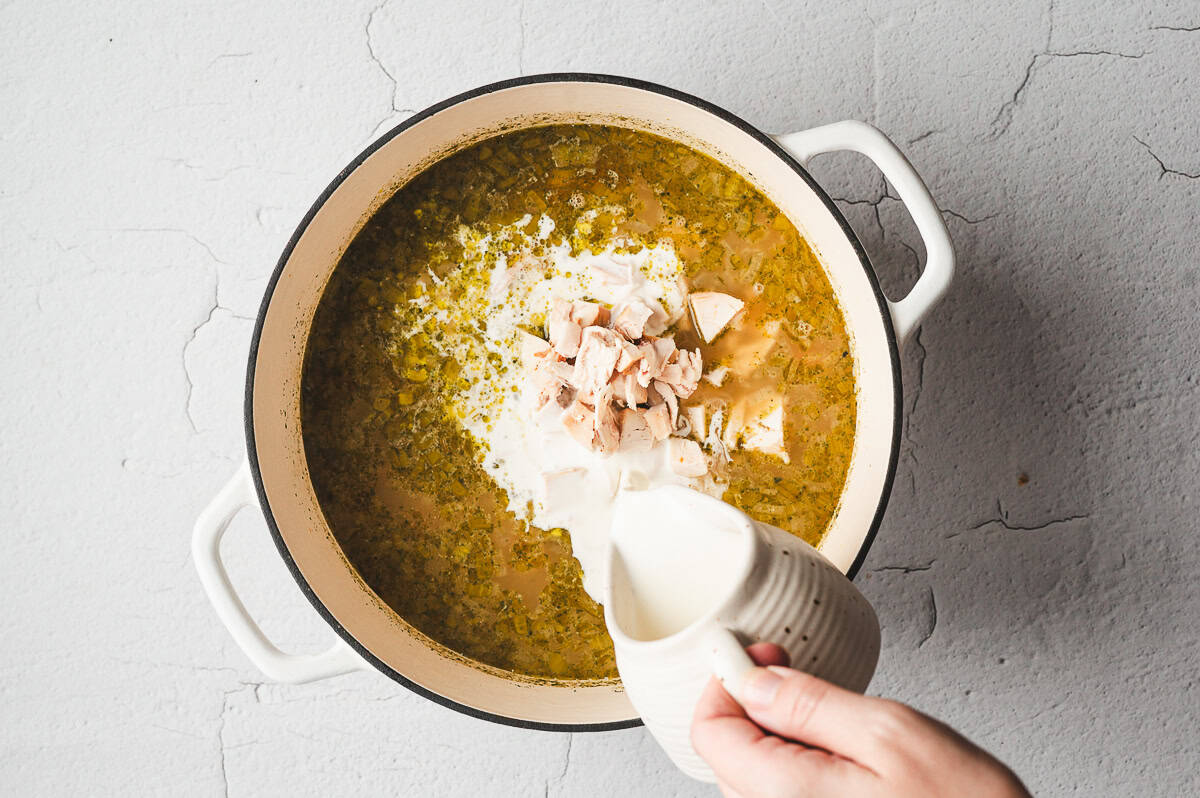cream being pour into soup pot with broth and chicken pieces