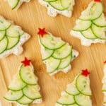 Festive Christmas tree cucumber sandwiches topped with red bell pepper stars on a wooden board.