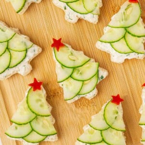 Festive Christmas tree cucumber sandwiches topped with red bell pepper stars on a wooden board.