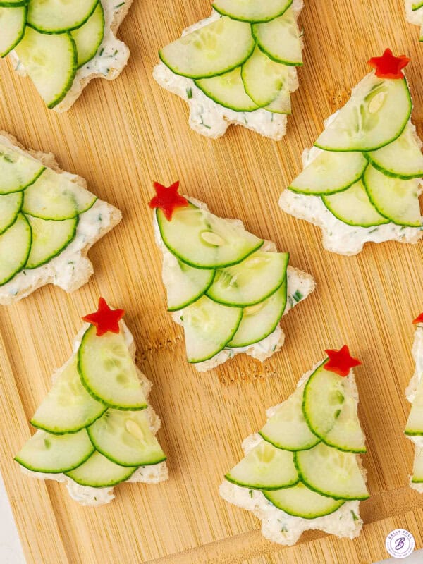 Festive Christmas tree cucumber sandwiches topped with red bell pepper stars on a wooden board.