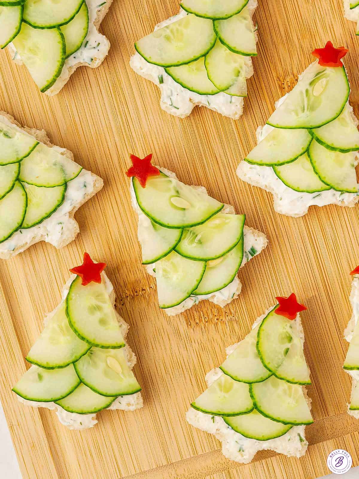 Festive Christmas tree cucumber sandwiches topped with red bell pepper stars on a wooden board.